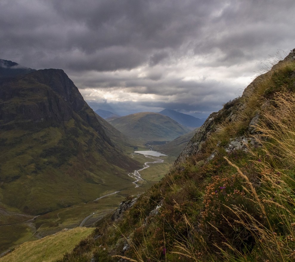 Dramatic view of the Glencoe valley in the Scottish Highlands, with dark, cloudy skies and sunlight breaking through over the mountains in the distance. ?? ''